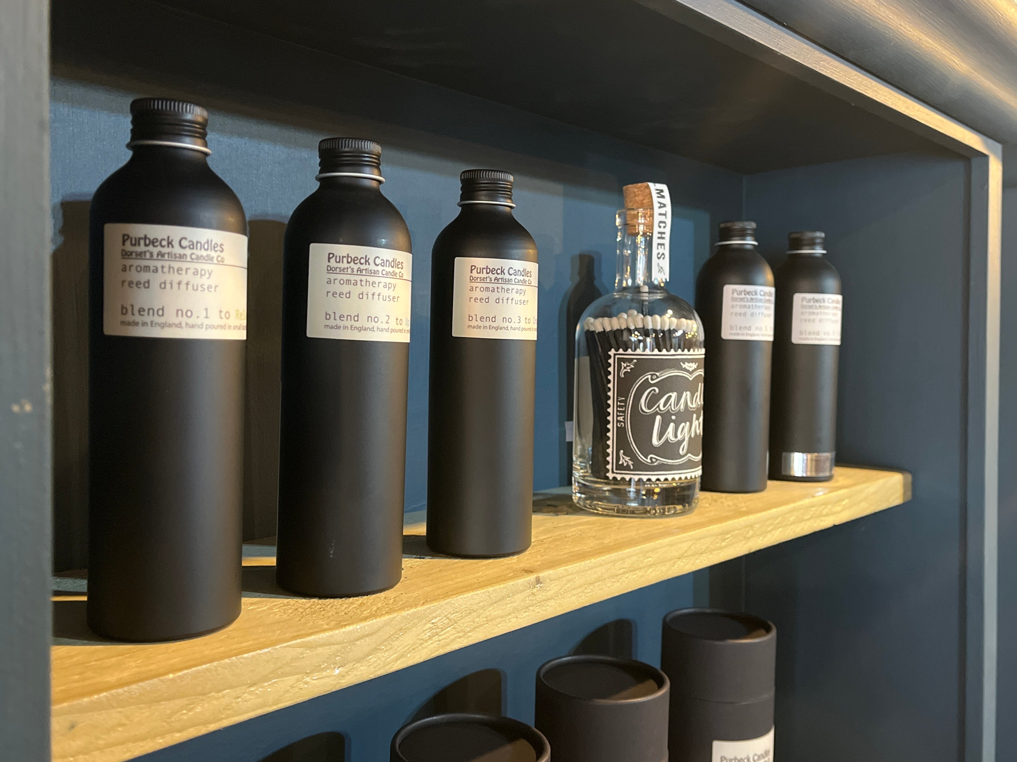 Collection of black bottles with labels on a wooden shelf against a blue wall.