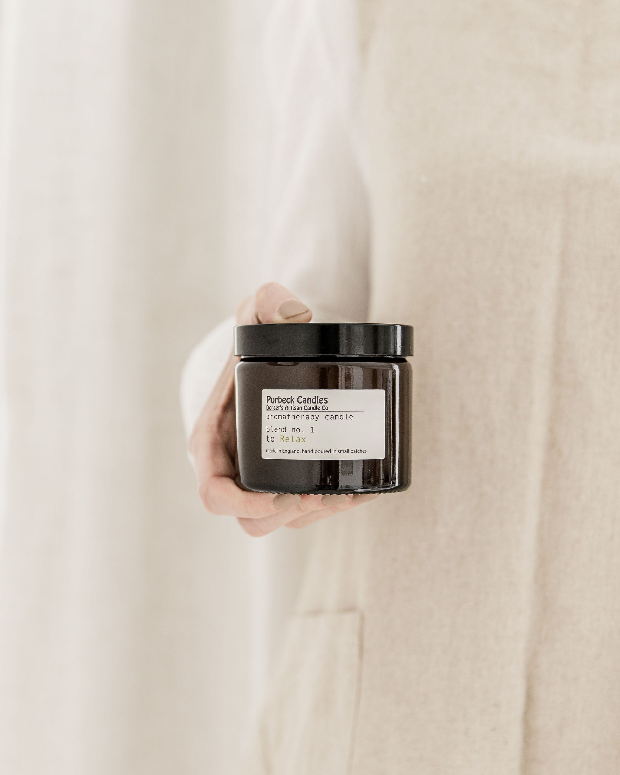 Hand holding a black candle jar with a white label against a beige background