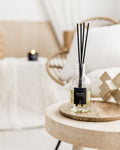 Boreas diffuser bottle with black sticks on a wooden table in a cozy room setting.