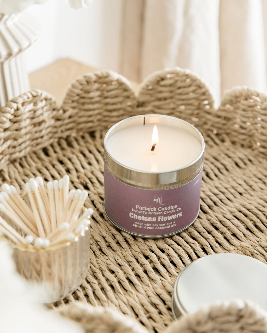 Candle in a purple container with a wick, surrounded by matches and a woven mat.