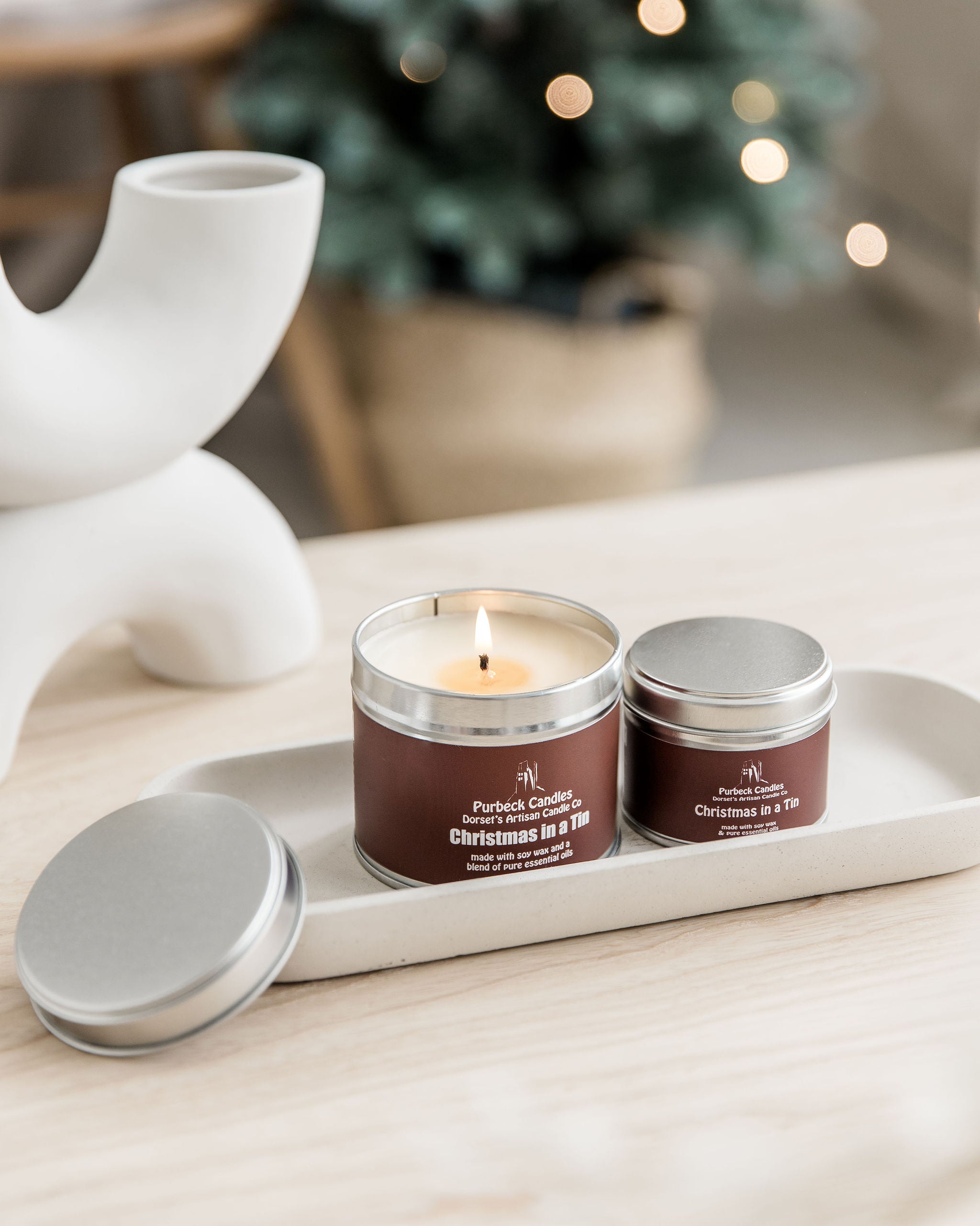 Two candles in metal tins on a white tray with a decorative background