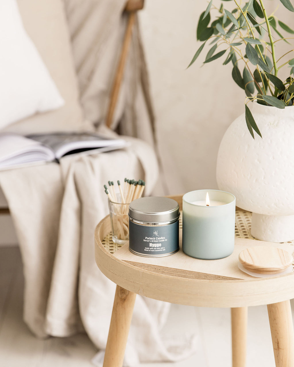 Candle and tin on a small wooden table with a plant in the background