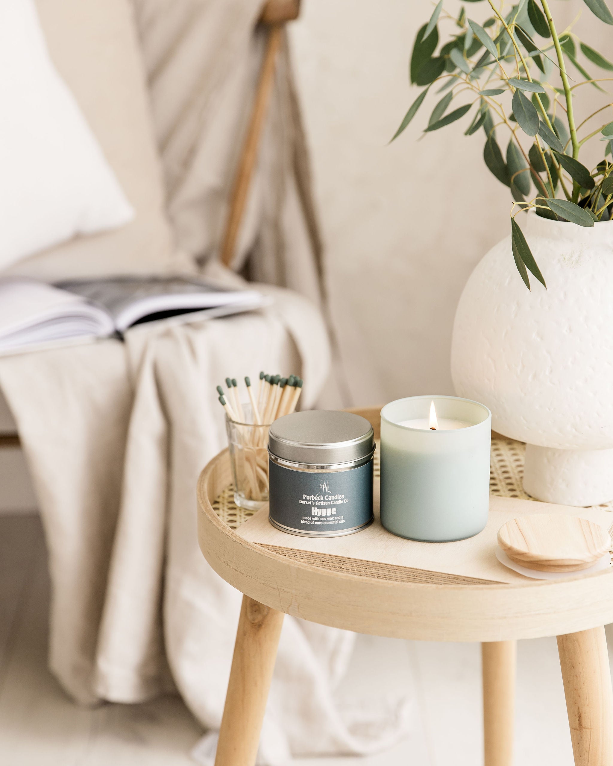 Candle and tin on a small wooden table with a plant in the background