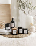 Collection of candles and bottles labeled 'living' on a textured surface with a plant in the background.