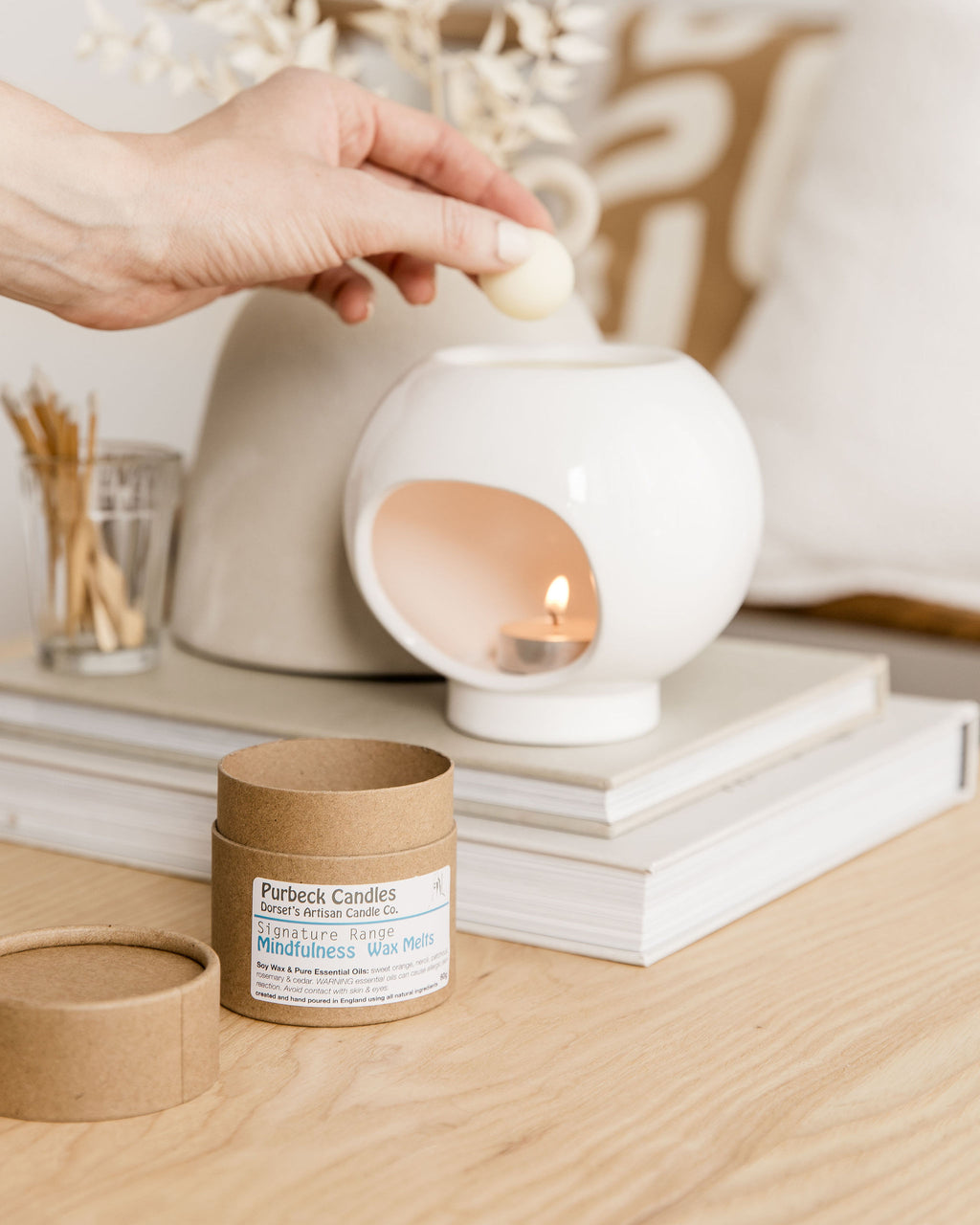 Person lighting a candle in a white ceramic holder with Purbeck Candles packaging on a wooden surface.