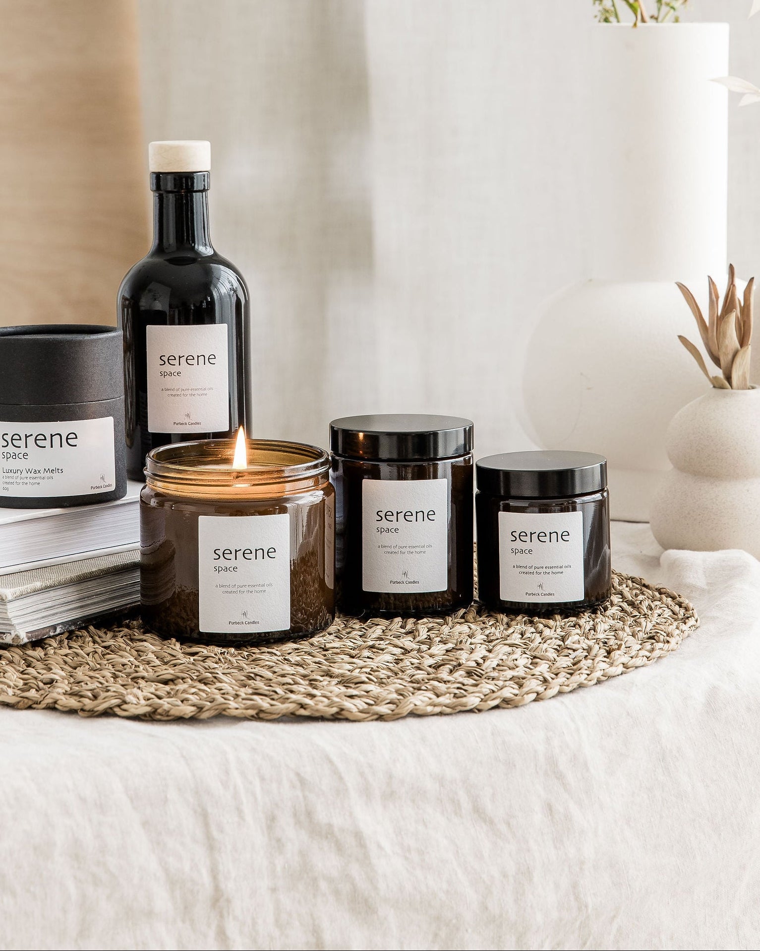 Collection of 'serene' branded candles and bottles on a textured surface with a neutral background.
