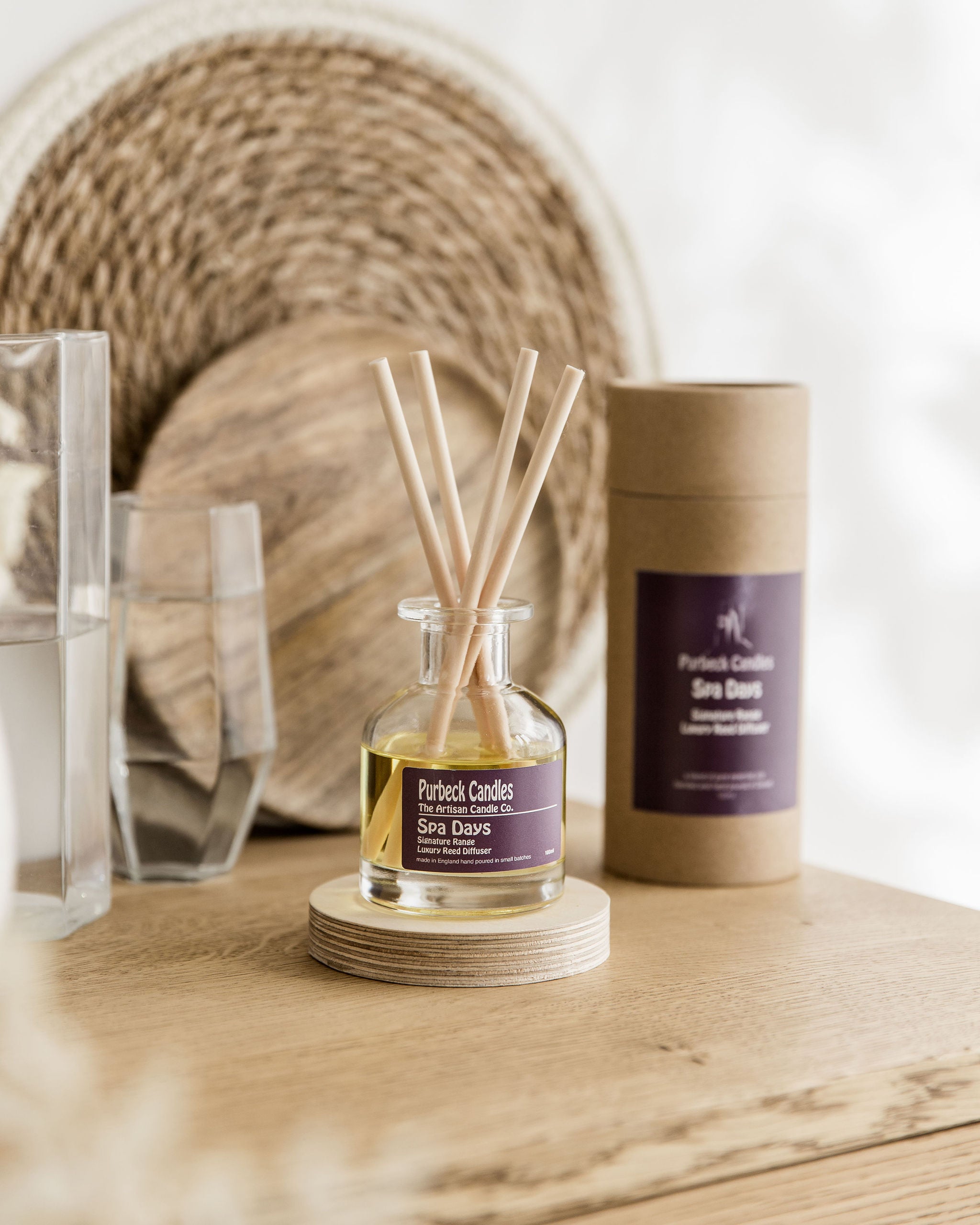Purbeck Candles reed diffuser and packaging on a wooden surface with a woven basket in the background.
