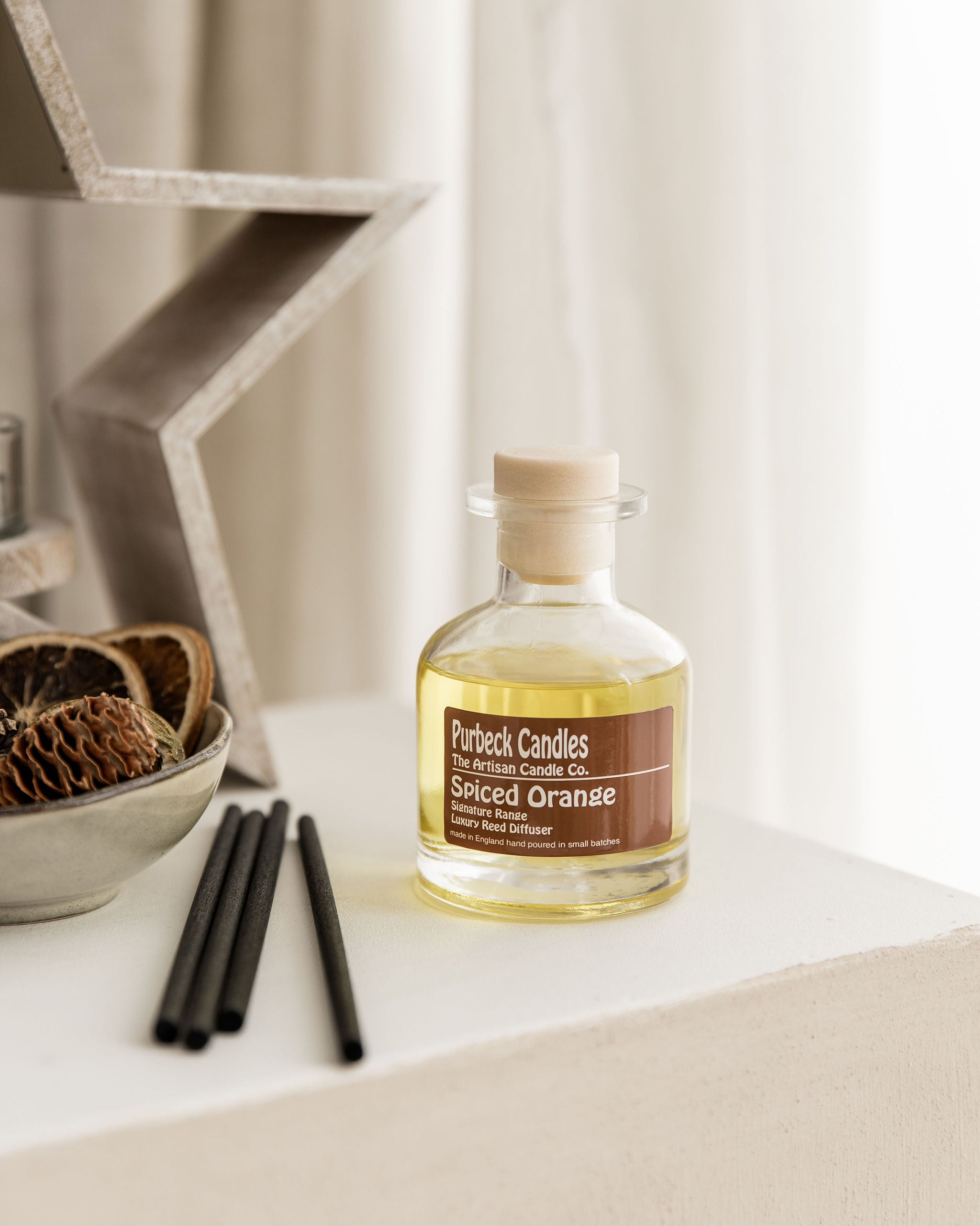 Bottle of Purbeck Candles Spiced Orange Diffuser on a surface with decorative items.