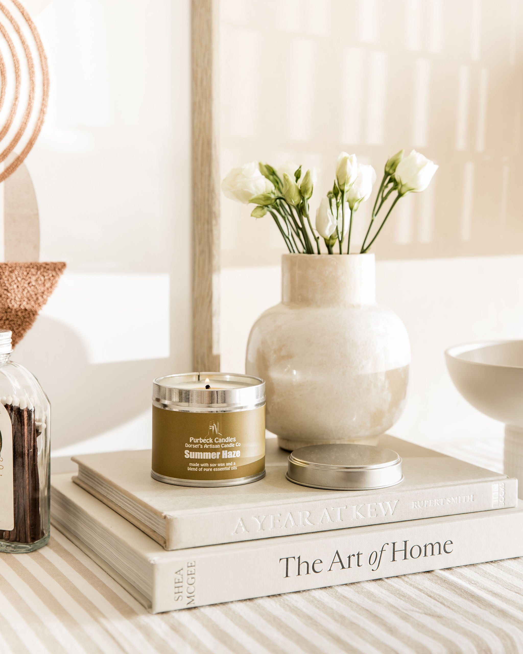 Candle, vase with flowers, and books on a surface with a neutral background