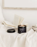 Zephyr candle in a black container on a white surface with a blurred background