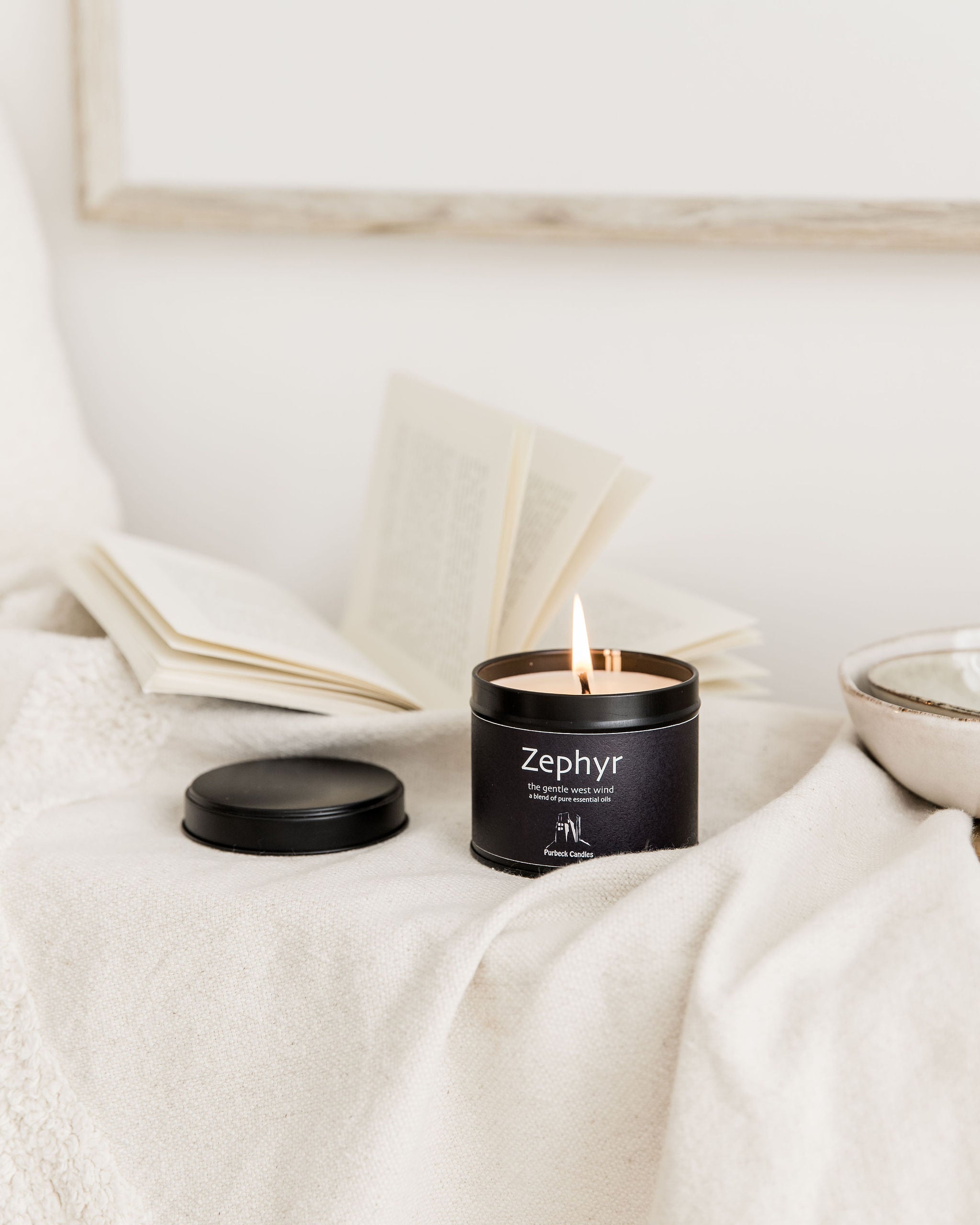 Zephyr candle in a black container on a white surface with a blurred background